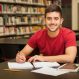 attractive-male-university-student-doing-some-homework-school-library-smiling_662251-1222