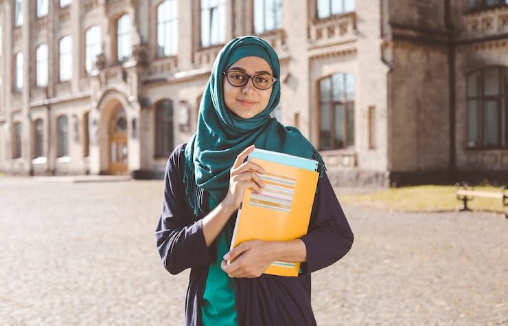 smiling-muslim-young-female-student-holding-books-standing-near-college-happy-arabian-girl-hijab-asian-woman-training_8119-2351